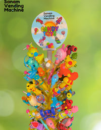 Colorful candy toy display with 'Sanam Vending Machine' branding against a green blurred background.